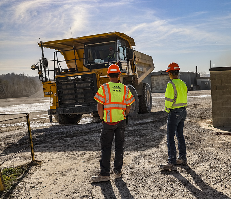 Two employees standing in the quarry in front of a big truck