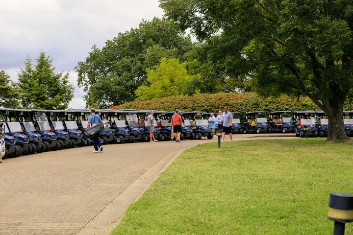 Participants walking beside a long row of golf carts at the start of the outing.