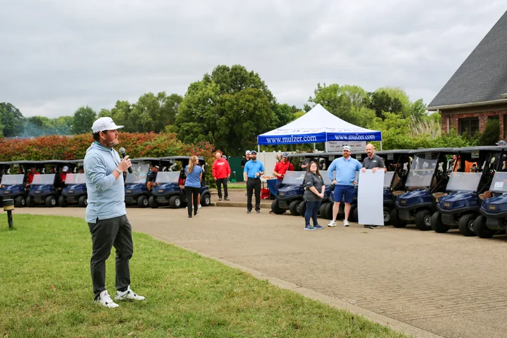 A participant addressing golfers near the registration tent and golf carts.