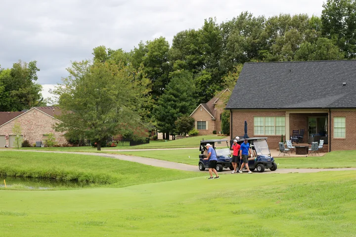 Golf carts passing a course building near the water.