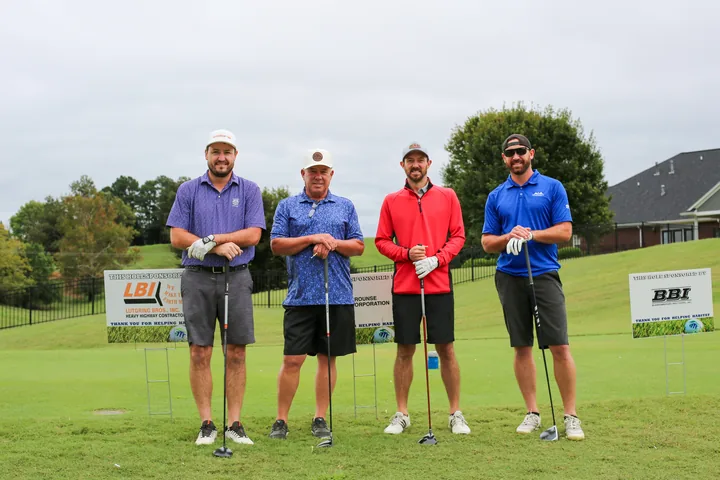A golf foursome in blue, red, and black shirts posing on the course.