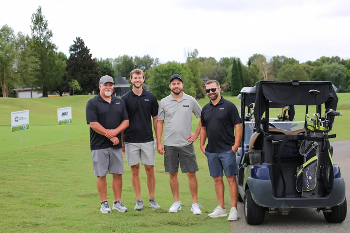 Four golfers posing beside a blue golf cart.