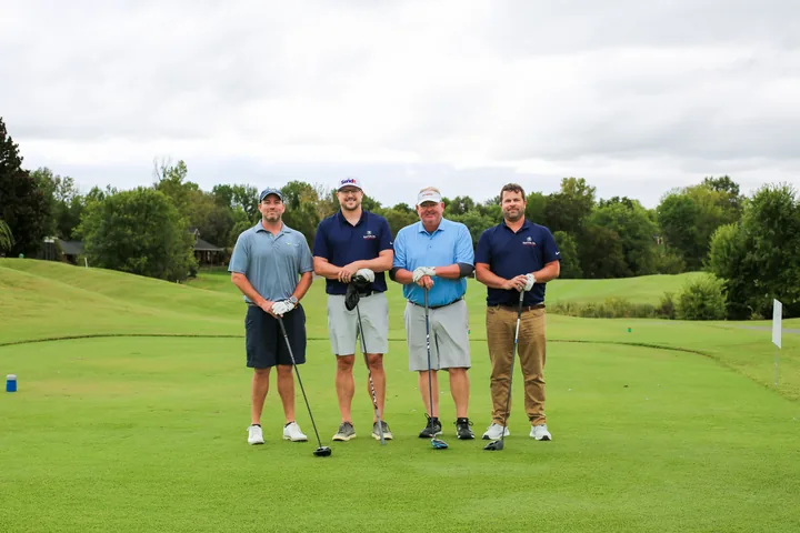 Four golfers in blue and navy shirts posing together on the green.