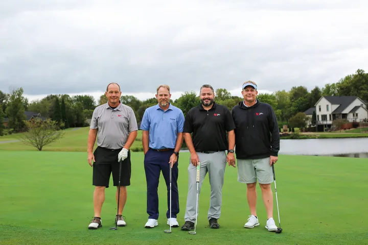Four golfers in gray, blue, and black shirts posing with their clubs.