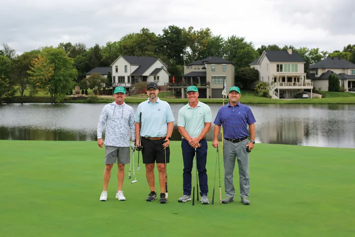 A foursome in pale gray, teal, and purple shirts posing by the lake.
