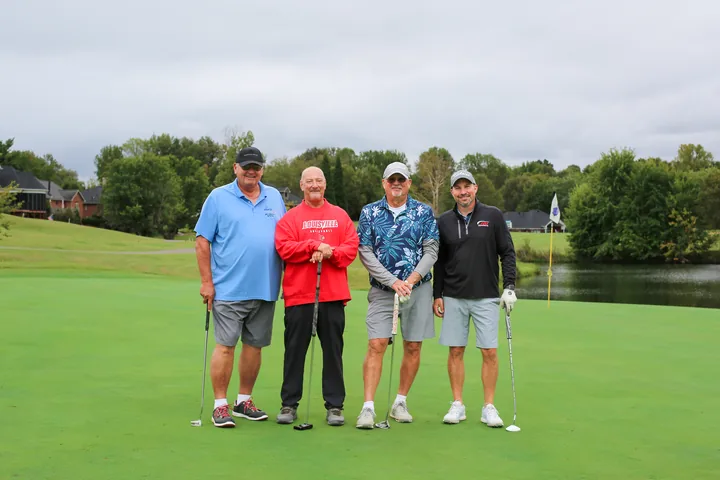 Four golfers in blue, red, patterned, and black shirts posing together.