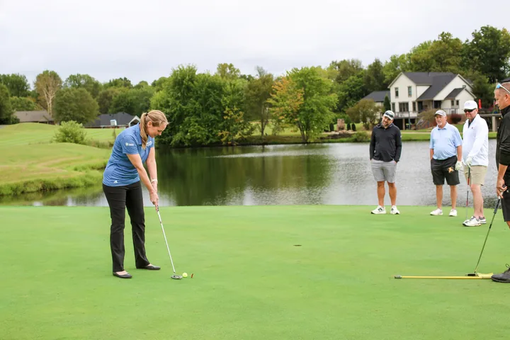 A participant preparing to putt while teammates watch near the lake.