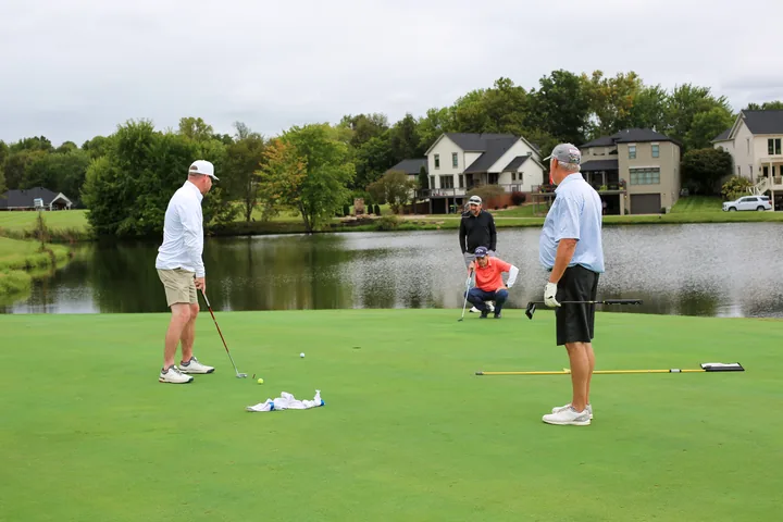 Participants discussing a putt on the green beside the lake.