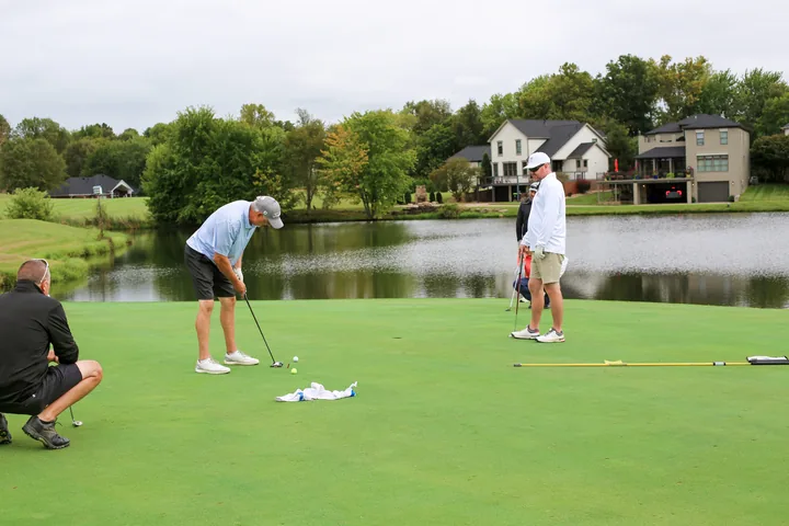 A golfer putting while teammates wait on the lakeside green.