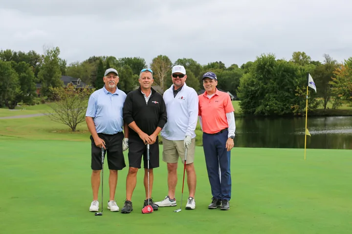 Four golfers in blue, black, white, and coral shirts posing with their clubs.