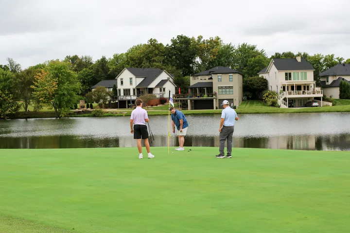 Three participants finishing play on a putting green beside the lake.